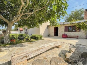A stone patio with a wooden bench, a tree, and a stone wall.