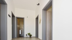 A hallway with light-colored tiled flooring, grey walls, and a door at the end leading to a room with a bed and a small plant. - Villa Meri by Interhome (Novigrad (Zadar))