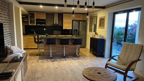 A modern kitchen with a bar area, a dining table, and a rocking chair. - Rez de Villa vue mer (Sari-Solenzara)