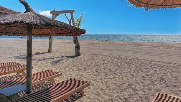 Une plage avec des chaises longues en bois et un parasol en chaume.