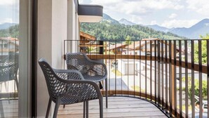 Un balcón con dos sillas de malla, una mesa de madera y vistas a montañas y un pueblo.