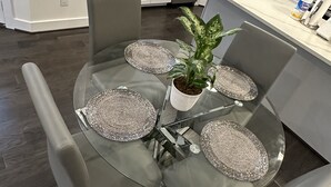 Una cocina moderna con armarios blancos, un lavamanos de acero inoxidable y una zona de comedor con mesa de vidrio y sillas grises.