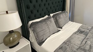Una cama con cabecera capitonada, dos almohadas y una lámpara de noche.