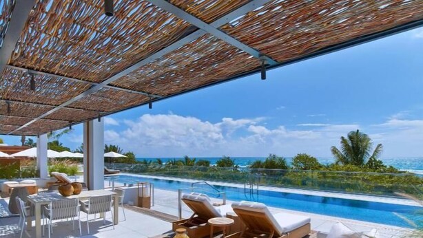 Uma área à beira da piscina com espreguiçadeiras, uma mesa com bebidas e vista para o oceano.