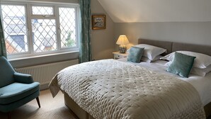 A bedroom with a large bed, a nightstand with a lamp, a chair, and a window with curtains. - East Park Lodge (Cowes)