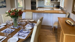 A modern kitchen with white cabinets, a wooden countertop, and a dining area set for six with a vase of flowers. - East Park Lodge (Cowes)