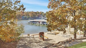 A lakeside view with a swing set, docked boats, and a building with a sloped roof. - Beautiful Main Channel View Cozy Condo in the HEART of Osage Beach! (Osage Beach)