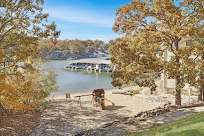 A lakeside view with a swing set, docked boats, and a building with a sloped roof.