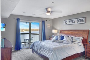 A bedroom with a bed, a 'NO WAKE ZONE' sign, a view of the outdoors, and a ceiling fan.