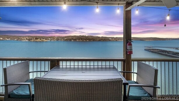 A covered outdoor seating area with a table and chairs, overlooking a body of water and a pier. - Beautiful Main Channel View Cozy Condo in the HEART of Osage Beach! (Osage Beach)