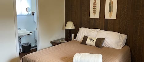 A neatly made bed with a quilted cover, a bedside lamp, and two framed pictures on the wall.