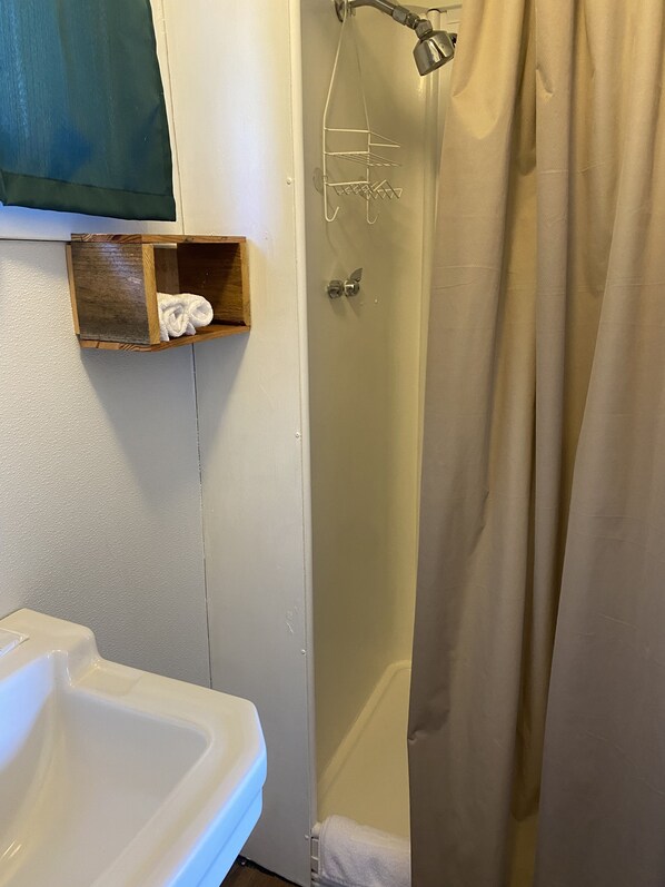 Une salle de bain avec un lavabo blanc, une étagère en bois sur laquelle est posée une serviette, et une douche avec un rideau beige.
