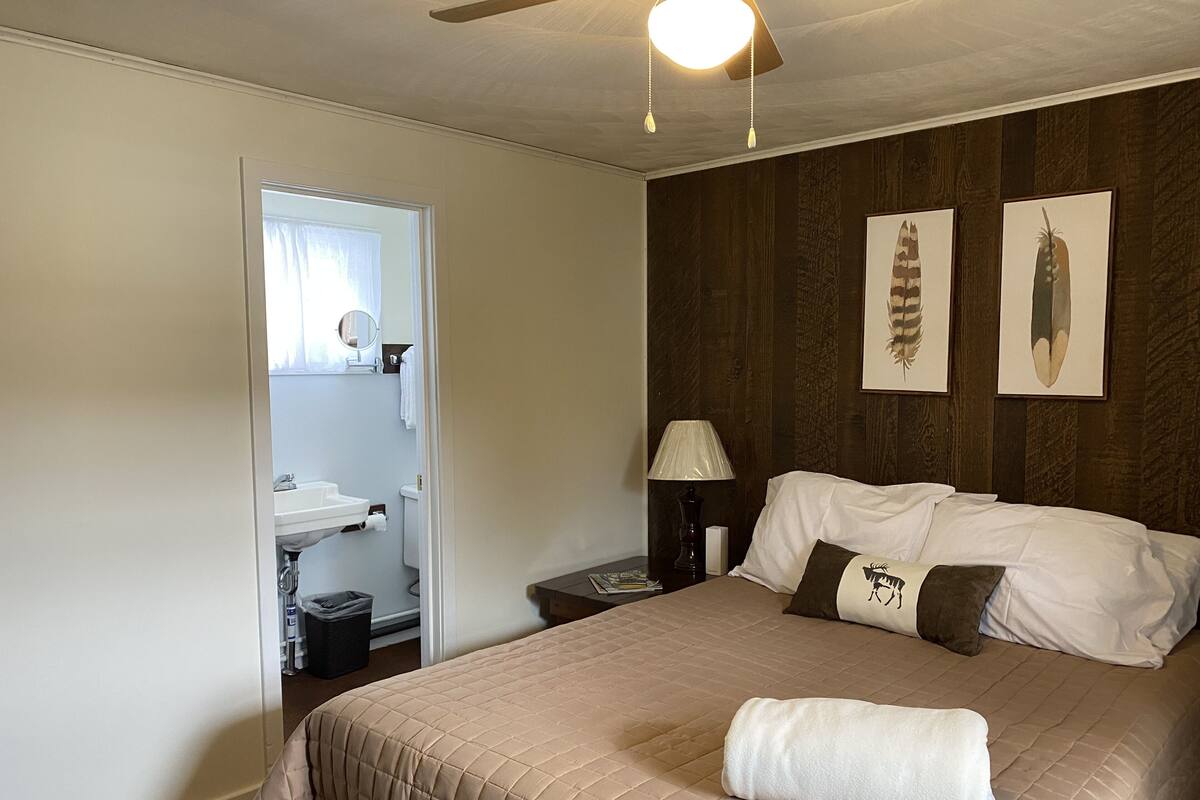 A hotel room with a bed, a nightstand, a lamp, a mirror, and a door leading to a bathroom.
