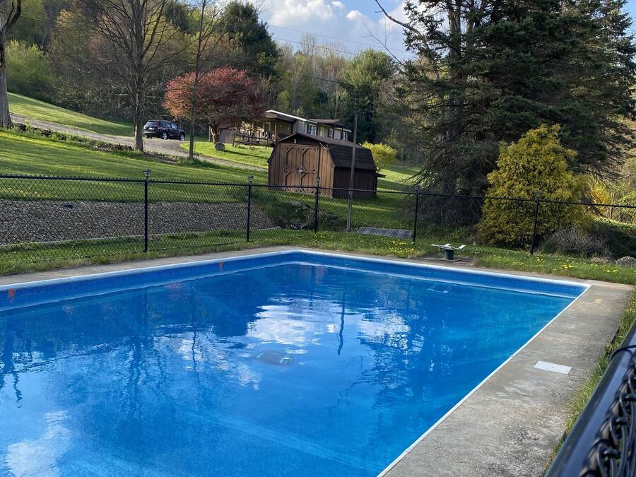 Ein rechteckiger Swimmingpool mit glasklarer, blauer Wasserfläche, umgeben von einem schwarzen Metallzaun.