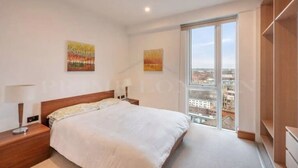 A modern bedroom with a large bed, two nightstands, a window with a city view, and two wall-mounted paintings. - Still Life Euston Deluxe (London)