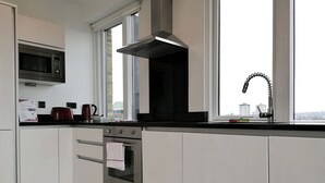 A modern kitchen with white cabinets, a built-in microwave, a stainless steel range hood, a double oven, and a window with a city view. - Still Life Euston Deluxe (London)