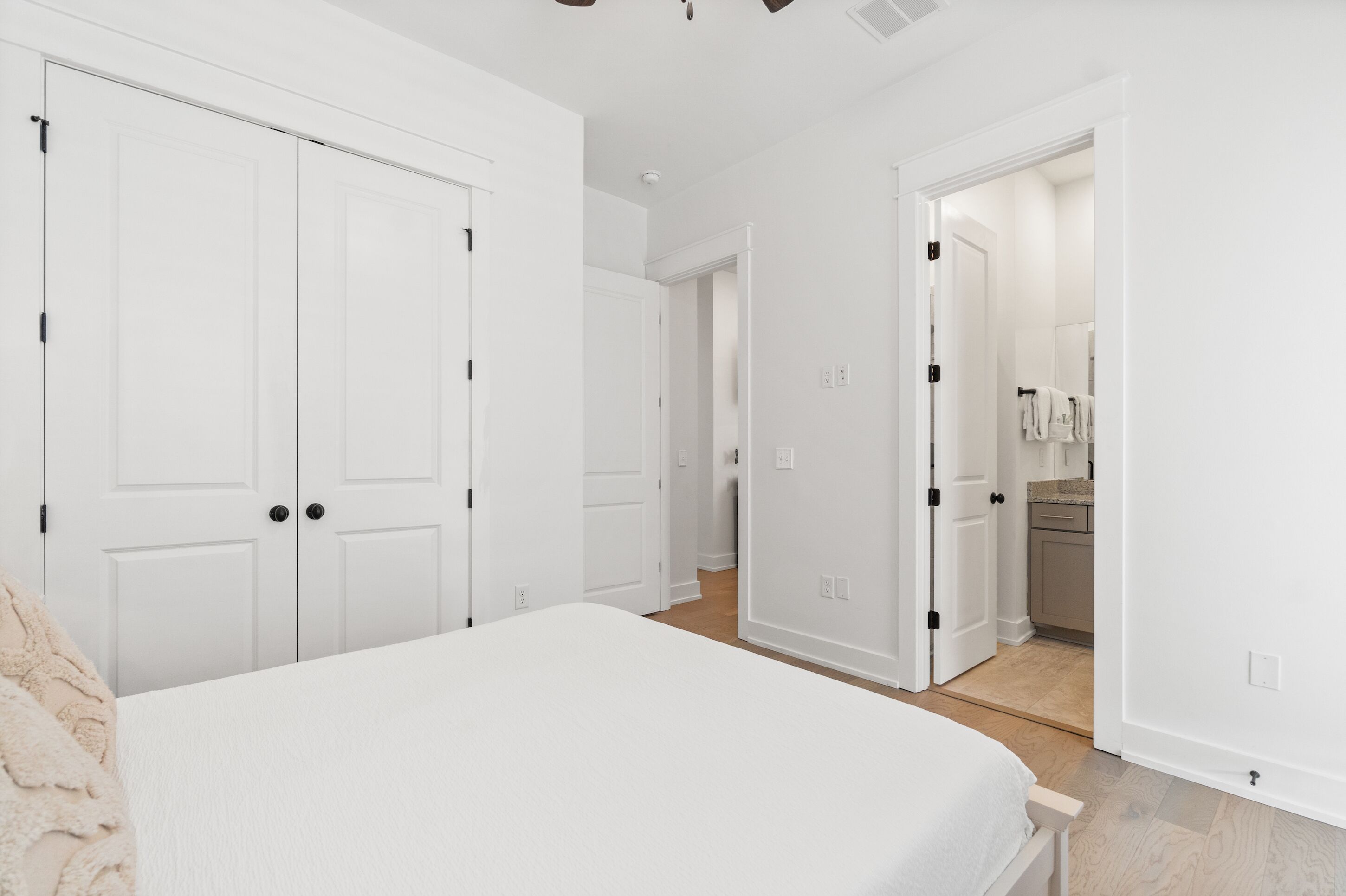 Un dormitorio con cama, armario blanco y baño visible a través de una puerta abierta.
