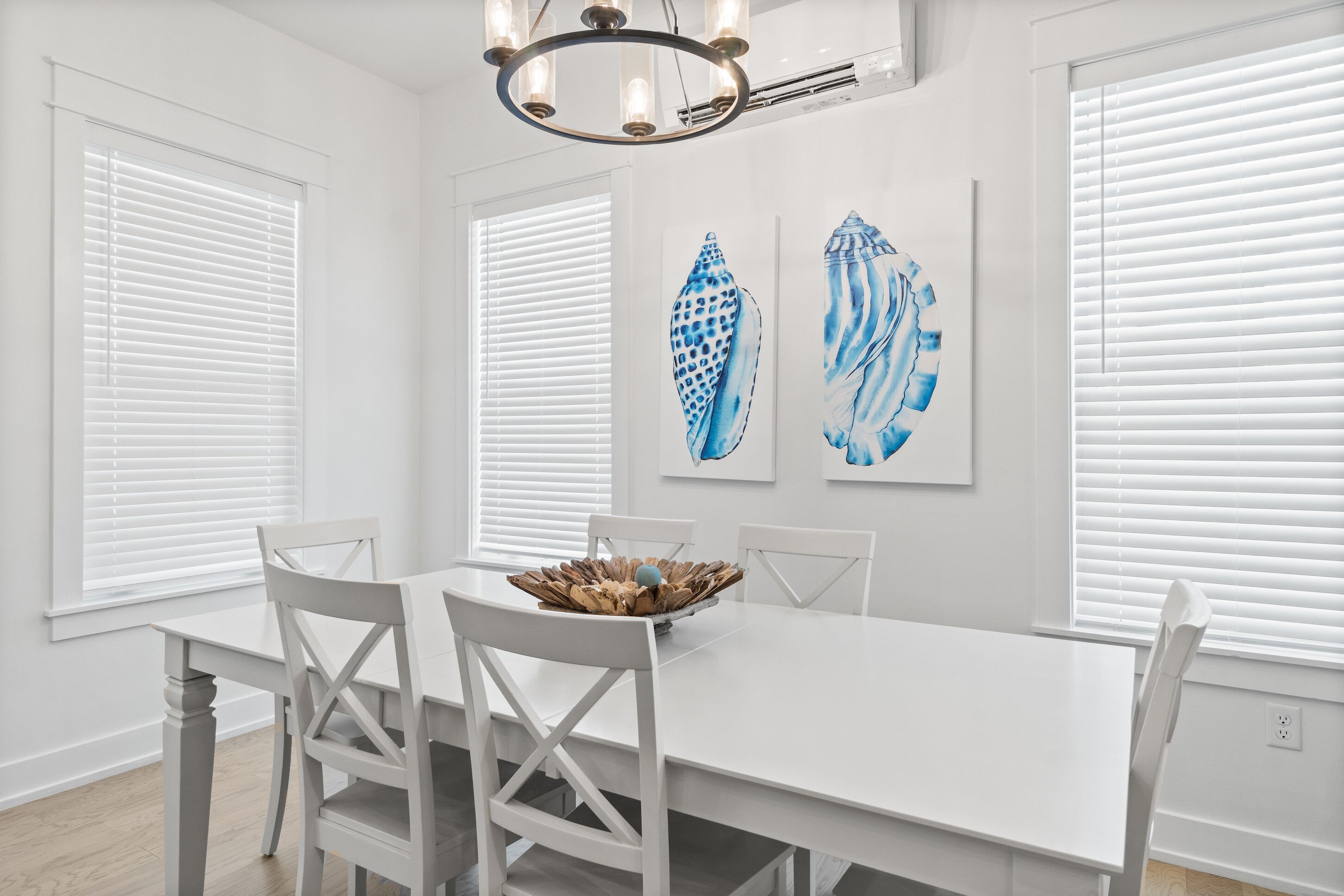 A dining area with a white table and chairs, a chandelier, and two framed artworks on the wall.