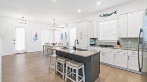 A spacious kitchen with white cabinetry, a central island with stools, a stainless steel refrigerator, and a chandelier. - 30A - The Charming Blue Haven by PHG (Santa Rosa Beach)