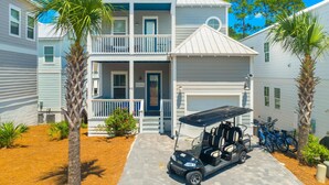 A two-story building with a balcony, a garage, and a golf cart parked in front. - 30A - The Charming Blue Haven by PHG (Santa Rosa Beach)