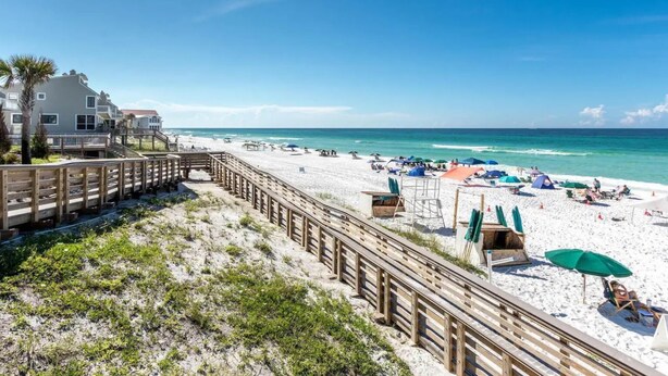 A beach with a wooden boardwalk, beach umbrellas, and a clear view of the ocean. - 30A - The Charming Blue Haven by PHG (Santa Rosa Beach)