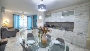 A modern living room with a sofa, a glass dining table set for four, and a kitchen with white cabinets and a marble countertop. - Spacious & modern 3 bedroom near seafront JBOR1-1 (Gzira)