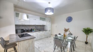 A modern kitchen with a central island, a dining area with a glass table, and a potted plant. - Spacious & modern 3 bedroom near seafront JBOR1-1 (Gzira)