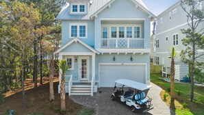 A two-story house with a garage, a covered porch, and a golf cart parked in front. - 30A Beach House - Harlies House by PHG (Panama City Beach)