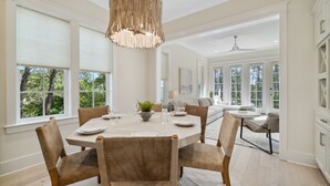 A dining area with a round table, chairs, and a hanging light fixture. - 30A Beach House - Harlies House by PHG (Panama City Beach)