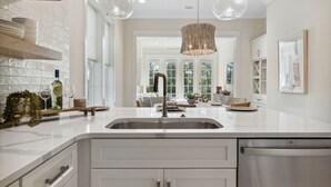 A modern kitchen with a white countertop, stainless steel sink, and a hanging light fixture. - 30A Beach House - Harlies House by PHG (Panama City Beach)