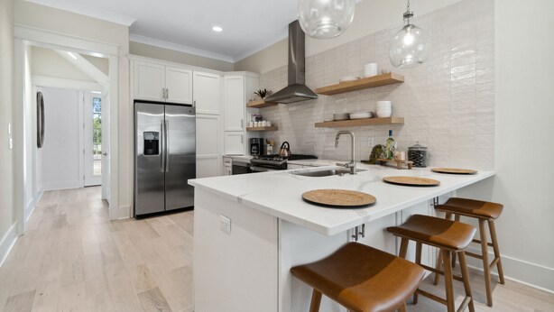 A modern kitchen with white cabinetry, a stainless steel refrigerator, a central island with stools, and pendant lighting. - 30A Beach House - Harlies House by PHG (Panama City Beach)