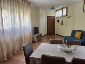 A living room with a TV, a dining table, and a blue sofa. - Sofia apartments (Firenze)