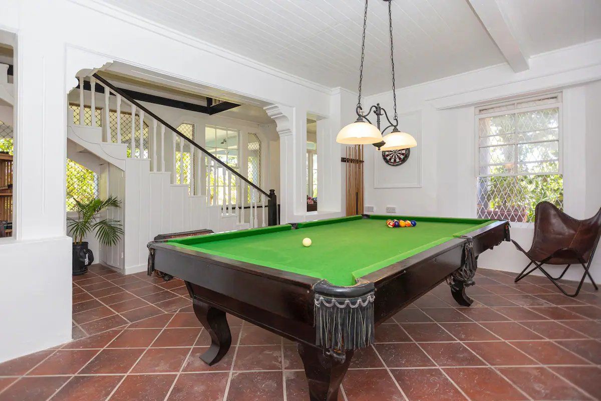 A pool table in a room with a staircase, a chair, and a hanging lamp.