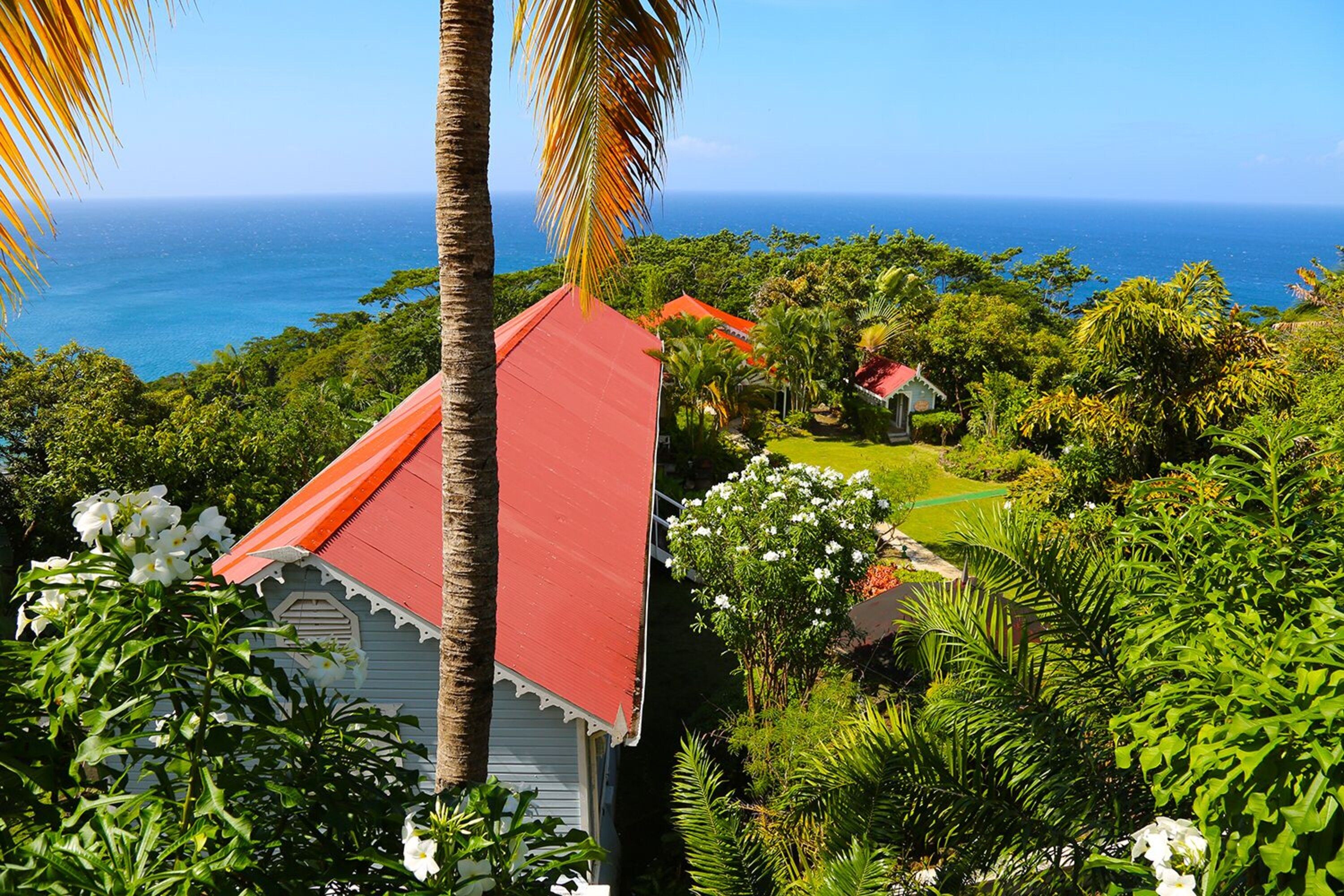 A coastal property with a red-roofed building surrounded by lush greenery and a view of the ocean.