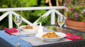 Une table à manger avec deux assiettes de nourriture, deux verres à vin et un vase rempli de fleurs.