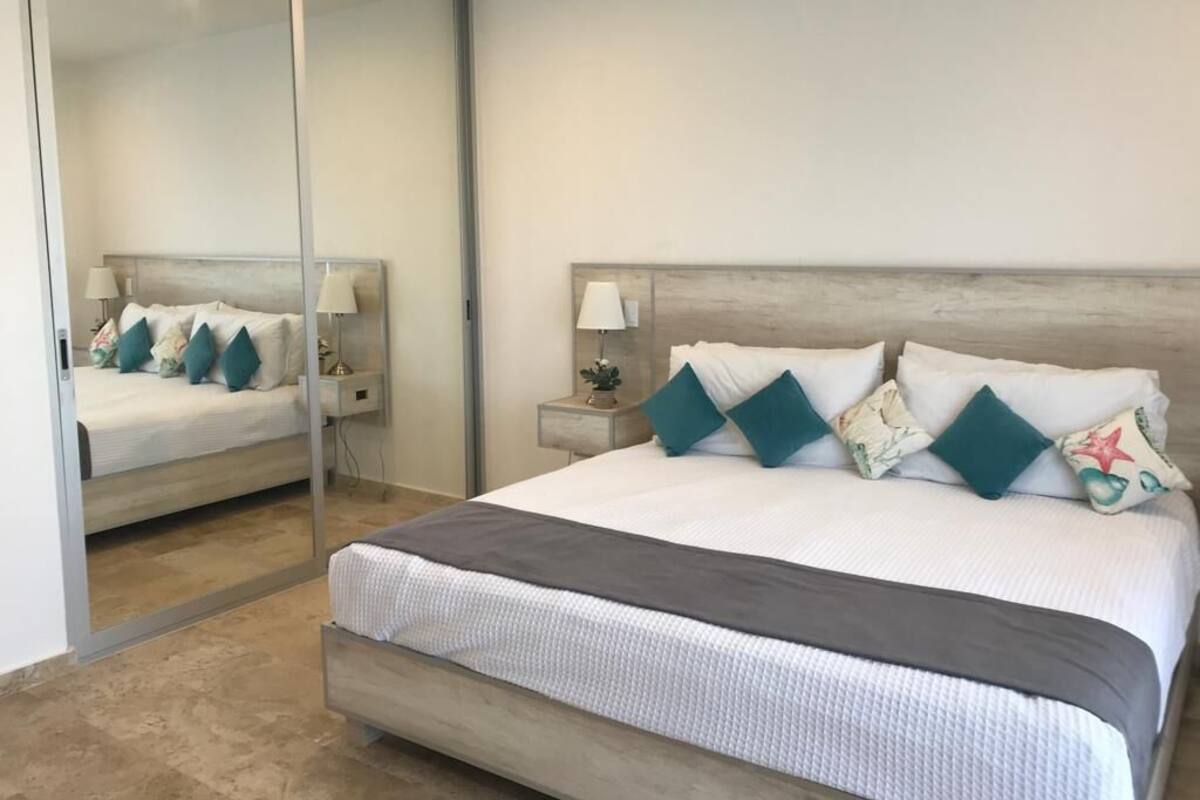 Ein modernes Schlafzimmer mit einem großen Bett, einem Nachttisch, einem Spiegel und einer Schiebetür.