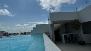 A modern swimming pool with a tiled edge, a covered seating area with chairs, and a staircase leading to an upper level. - Kuyaan 44 Suites (Playa del Carmen)