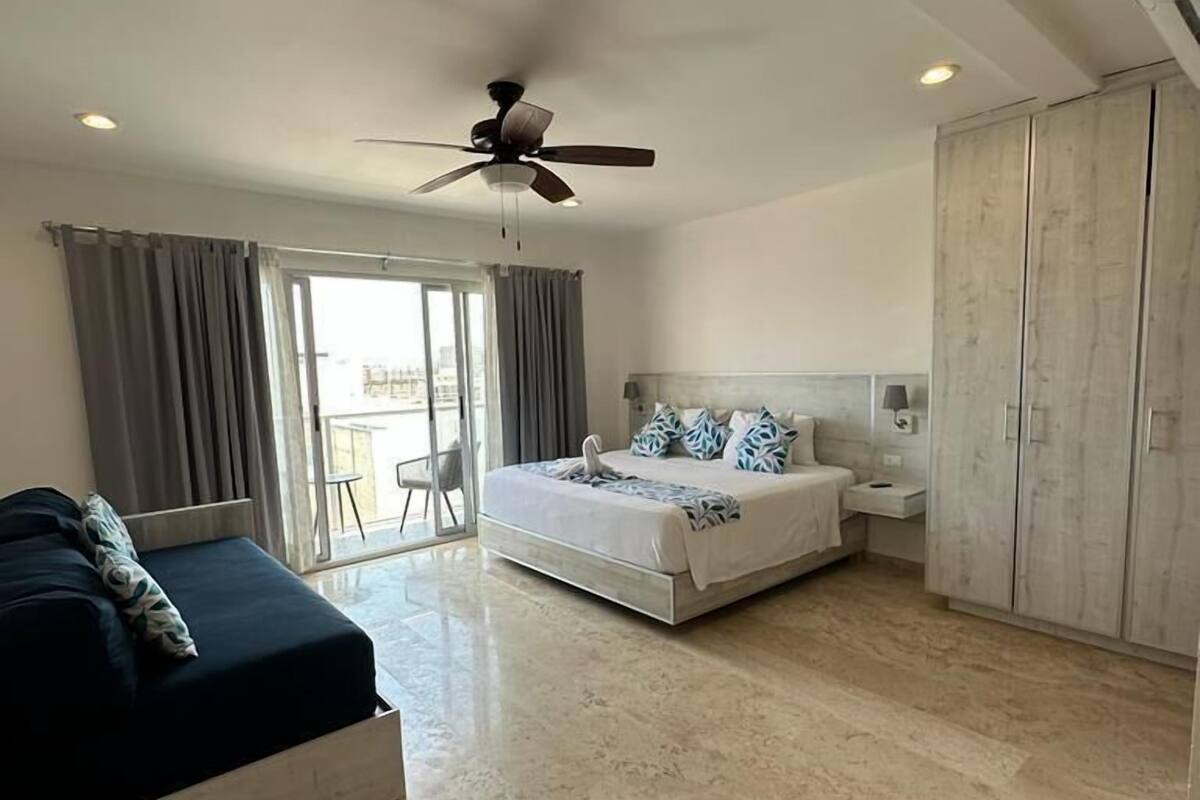 A bedroom with a bed, a wardrobe, a ceiling fan, and a view through a window.