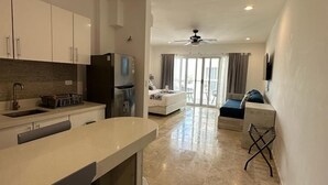 A modern kitchen with a central island, a dining area with a high table, and a living room with a sofa and a TV. - Kuyaan 44 Suites (Playa del Carmen)
