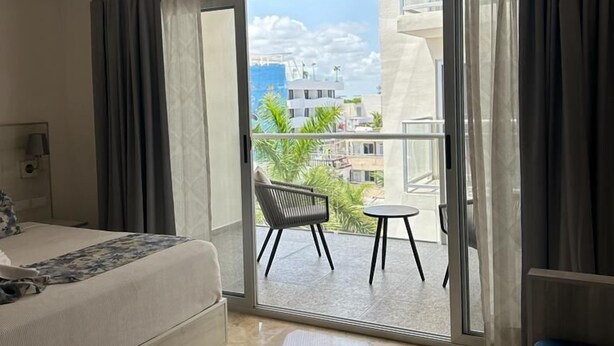 A hotel room with a bed, a small table, and a chair on a balcony with a city view. - Kuyaan 44 Suites (Playa del Carmen)