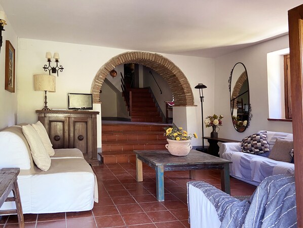 Ein Wohnzimmer mit einer Couch, einem Couchtisch mit Blumen, einem Fernseher und einer Treppe, die zu einer oberen Etage führt.