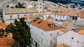 A historic cityscape with stone buildings and terracotta roofs, featuring a prominent tower and a fortified wall.