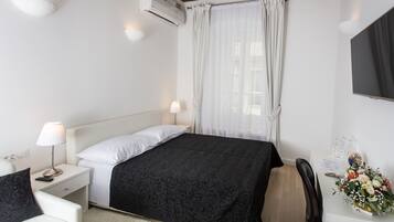 A hotel room with a bed, bedside lamps, a desk with a computer, a chair, a TV, and a window with curtains.