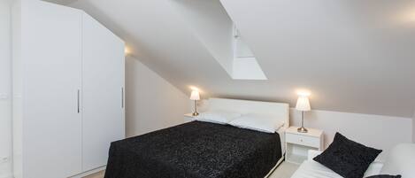 A modern bedroom with a skylight, a bed with black bedding, a white wardrobe, and bedside lamps.