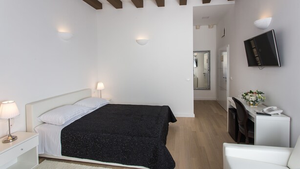 A bedroom with a bed, bedside lamps, a desk with a chair, a TV, and a small table with a vase of flowers.
