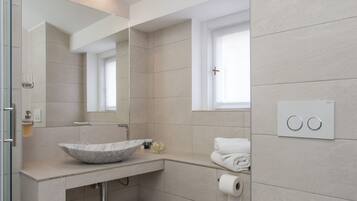 A modern bathroom with a vessel sink, a toilet, a trash can, and a window.