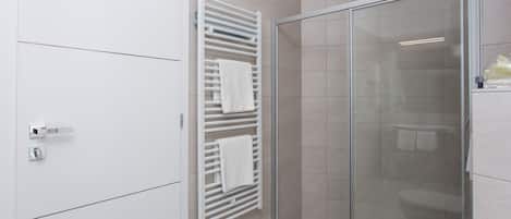 A modern bathroom with a glass shower enclosure, a white toilet, and a towel rack with folded towels.
