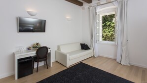 A modern room with a white sofa, a desk with a chair, a flat-screen TV, and a window with curtains.