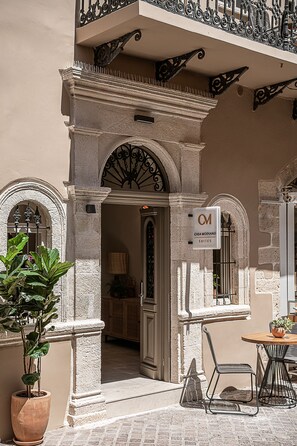 An entrance with a sign for 'Casa Modiano Suites', a potted plant, and a table with chairs outside. - Casa Modiano (Chania)