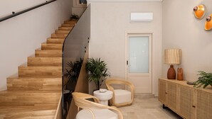 A modern interior with a wooden staircase, wicker chairs, a small table, and a cabinet with decorative items. - Casa Modiano (Chania)